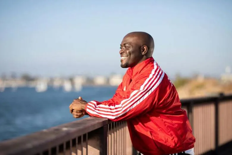Hombre sonriendo apoyado en una barandilla junto al mar
