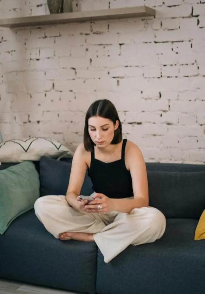 Mujer sentada en un sofá escribiendo en su teléfono